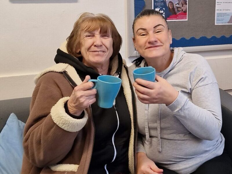 two people in cafe holding mugs of coffee smiling